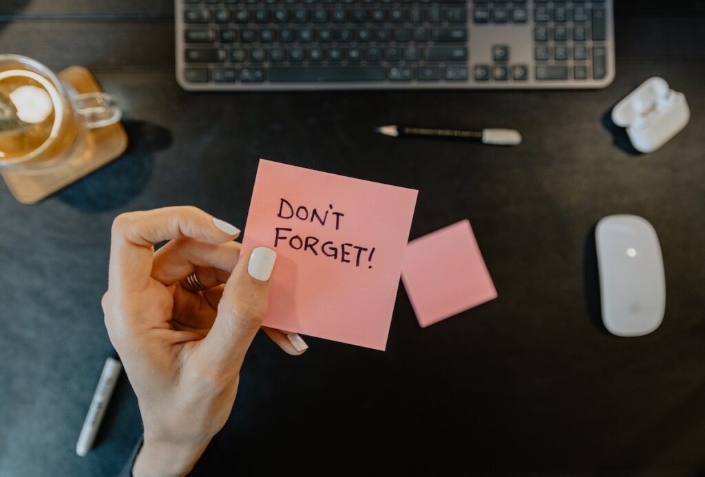Image shows a hand holding a post-it that reads "Don't Forget!" Just like someone like me, with poor working memory and executive function problems.